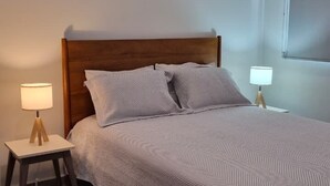 A bedroom with a bed, bedside lamps, a wooden floor, and an air conditioning unit. - Relax, Unwind and Experience Vallarta (Puerto Vallarta)