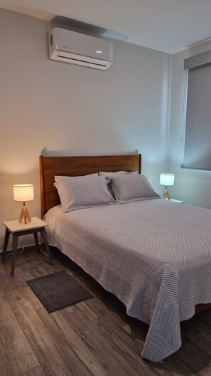 A bedroom with a bed, bedside lamps, a wooden floor, and an air conditioning unit. - Relax, Unwind and Experience Vallarta (Puerto Vallarta)