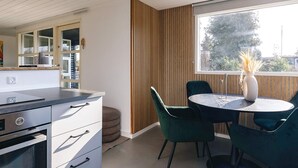 A modern kitchen with a built-in oven, a dining area with a round table and green chairs, and a large window with a view of trees. - 4 Star Holiday Home in Faxe Ladeplads (Faxe Ladeplads)