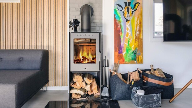 A modern living room with a wood-burning stove, a grey sofa, a colorful abstract painting, and a TV mounted on the wall. - 4 Star Holiday Home in Faxe Ladeplads (Faxe Ladeplads)