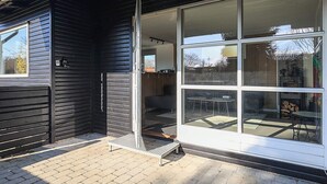 A modern building with a large glass door, a metal step leading to the entrance, and a brick-paved area outside. - 4 Star Holiday Home in Faxe Ladeplads (Faxe Ladeplads)
