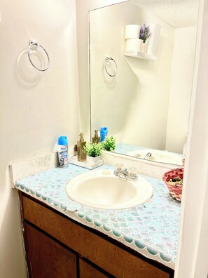 A bathroom with a white sink, a mirror, and a towel rack. There is a blue bottle on the counter and a small plant.