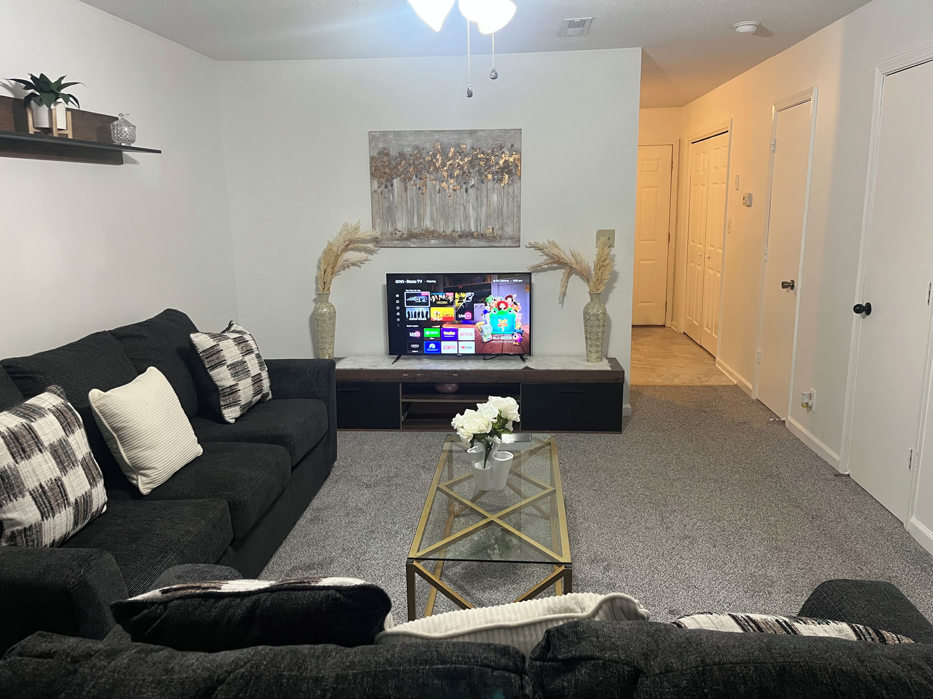 Una sala de estar con un sofá, una mesa de centro, un televisor de pantalla plana y un pasillo que conduce a una puerta.