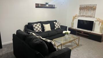Un soggiorno con un divano nero, un tavolino in vetro, una televisione a schermo piatto e una ventola a soffitto.