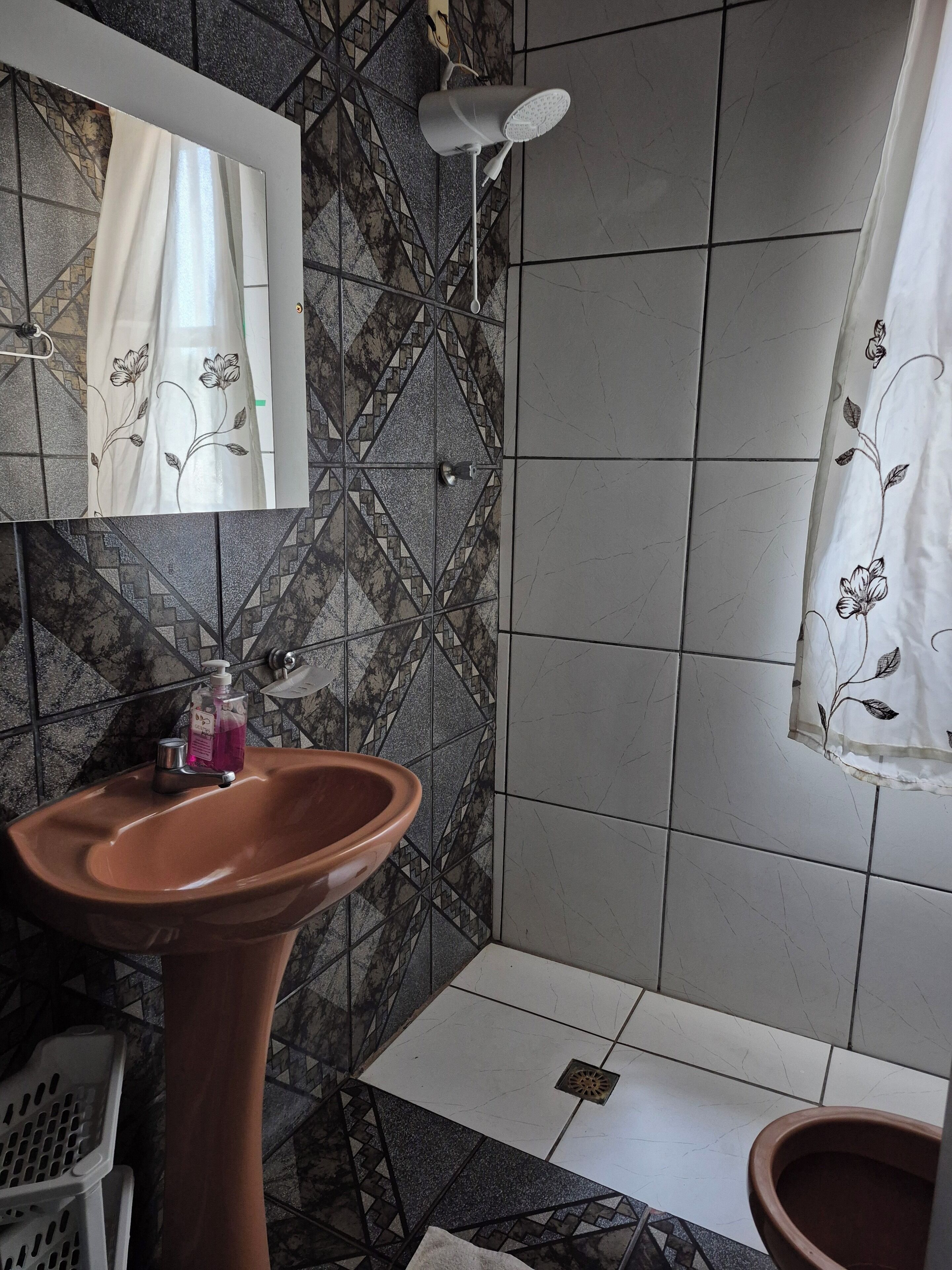 A bathroom with a pedestal sink, a mirror, a shower with a white shower curtain, and patterned tiles.