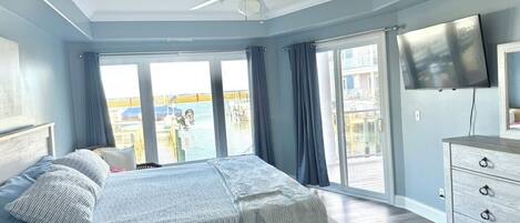 Un dormitorio con cama, ventilador de techo, televisión y vista al exterior.