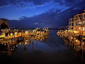 A marina at dusk with calm water reflecting the lights, docked boats, and buildings with balconies. - THIS MUST BE THE PLACE! Captain Beebe's waterfront condo (Chincoteague)
