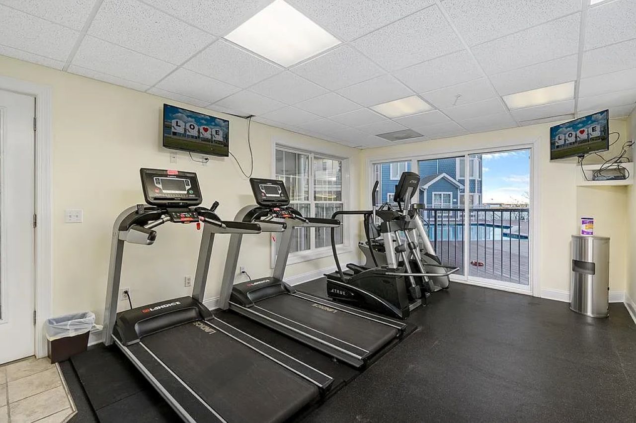 A gym with treadmills, ellipticals, and a TV screen displaying 'LOVE'.
