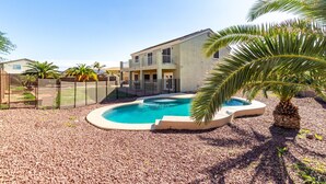 A two-story house with a swimming pool surrounded by pebbles.