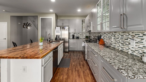 A modern kitchen with grey cabinets, a wooden island, and a tiled backsplash.