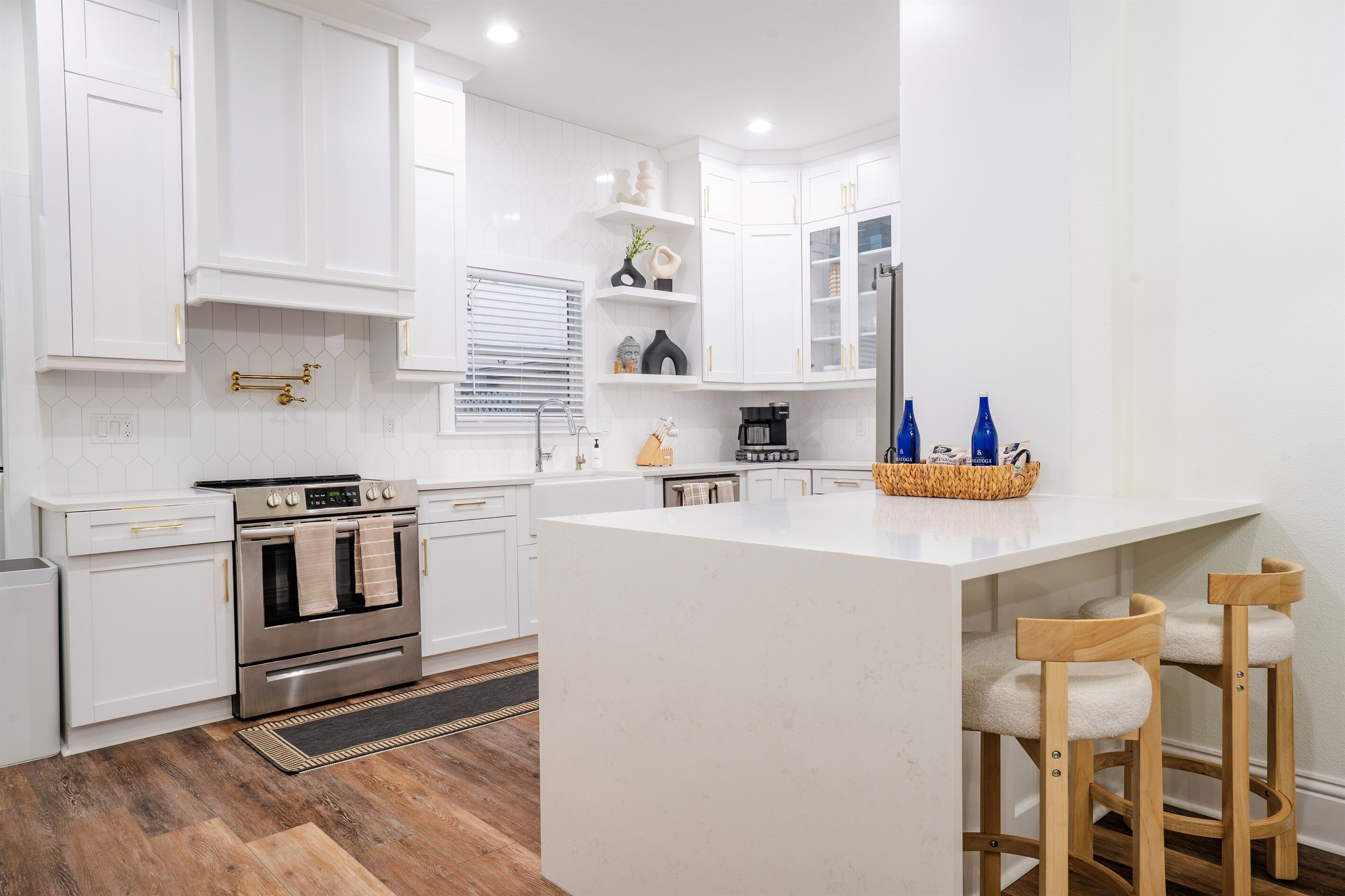Une cuisine moderne avec des meubles blancs, un îlot central et des tabourets de bar en bois.