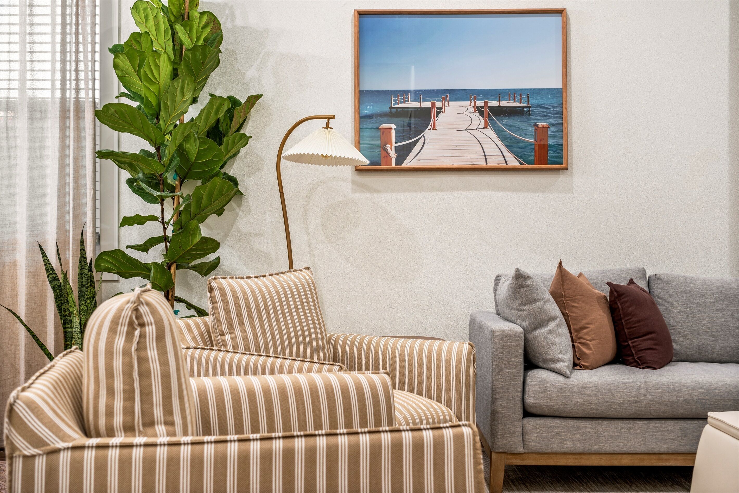 Ein Wohnzimmer mit gestreiften Sofas, einem grauen Sofa und einer großen Pflanze.