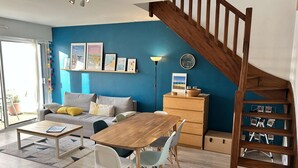 Een woonkamer met een houten trap, een bank, een eettafel met stoelen en een kast.