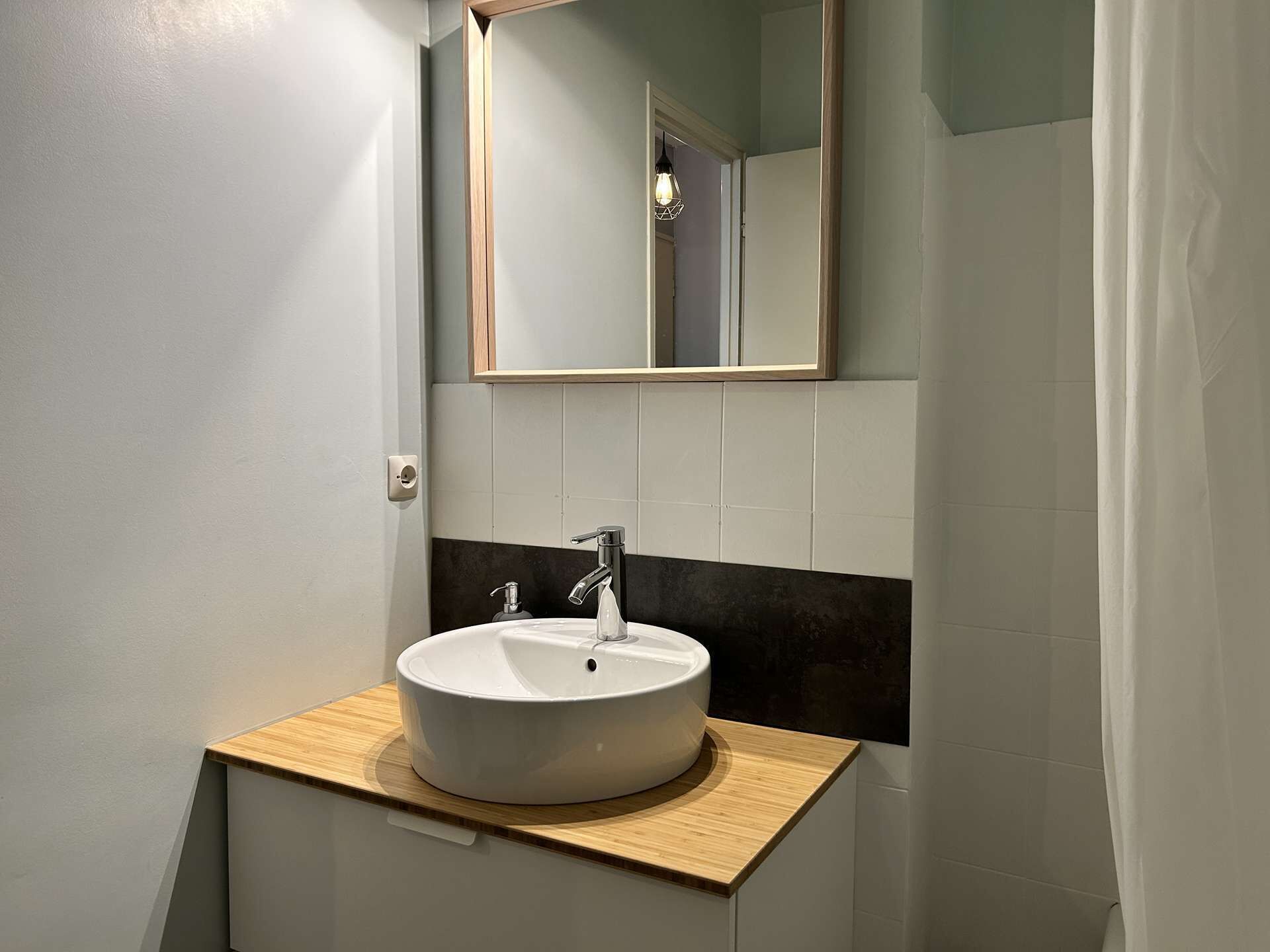Une salle de bain avec un lavabo blanc, un plan de toilette en bois et un miroir au-dessus.