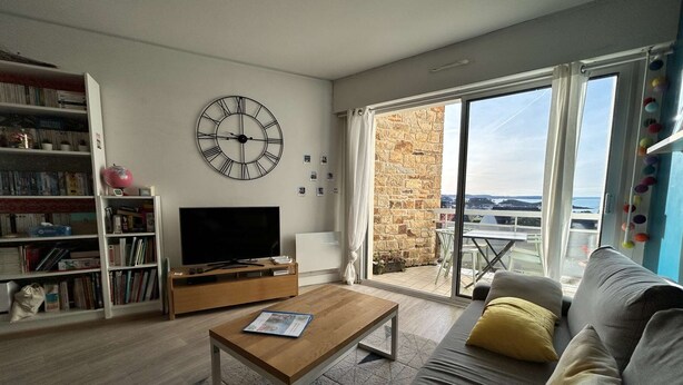 Een moderne woonkamer met een flatscreen televisie, een houten salontafel, een bank met kussens, een boekenkast en een grote wandklok.