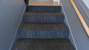 Een trap met donkerbezuilde treden, een houten leuning en een lichtgekleurde muur met verticale panelen.
