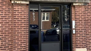Een bakstenen gebouw met een zwarte glazen deur, huisnummer 503, en een klein raam erboven.