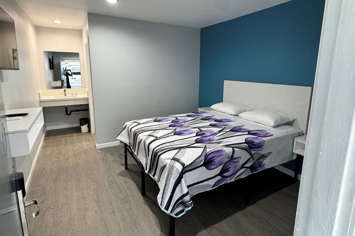 Un dormitorio con cama, mesita de noche, tocador y baño con lavamanos y espejo.