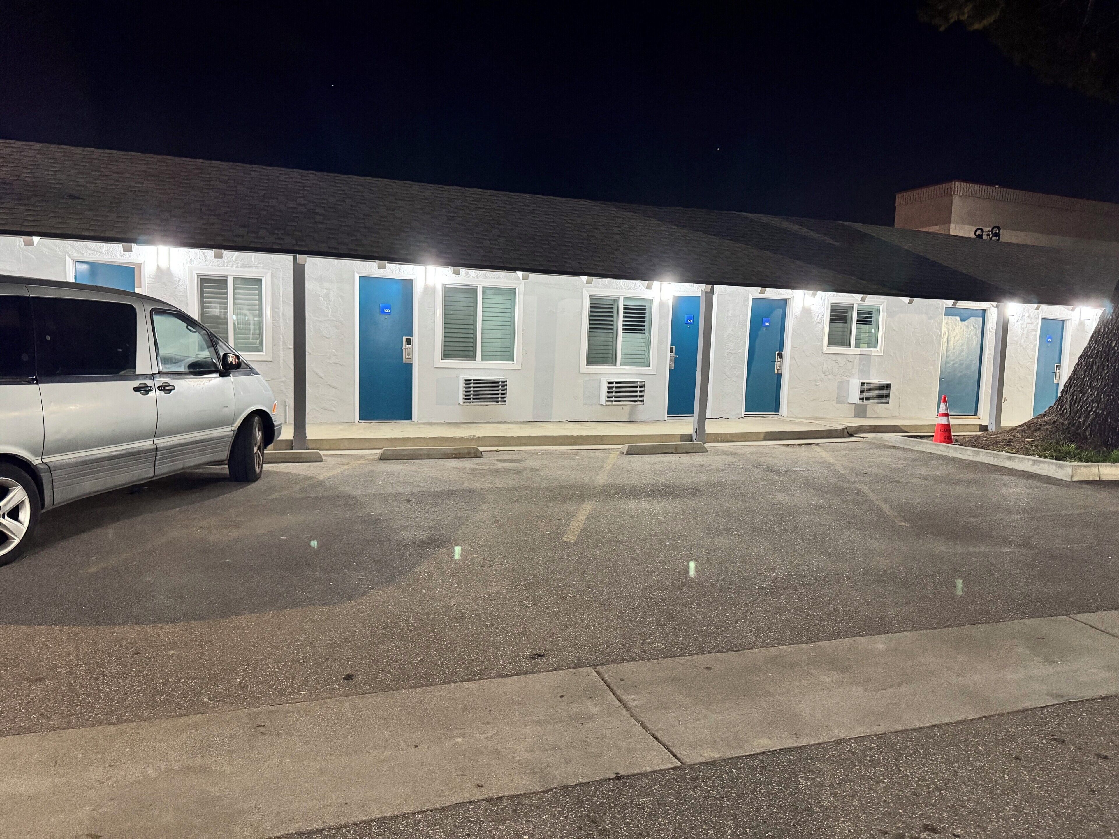 A motel with a parking lot, multiple rooms with blue doors, and a white exterior.