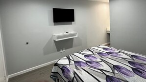 A bedroom with a bed, a mounted TV, a small white bedside table, and a wall-mounted sink. - Angel Motel near Anaheim  (Orange)