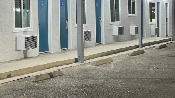 A row of hotel rooms with individual air conditioning units, numbered doors, and a concrete floor. - Angel Motel near Anaheim  (Orange)