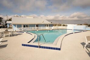 A swimming pool with a white fence, lounge chairs, and a building with a blue roof in the background. - Starr Estates Marvel House Sunretreat Rv Park (Kissimmee)