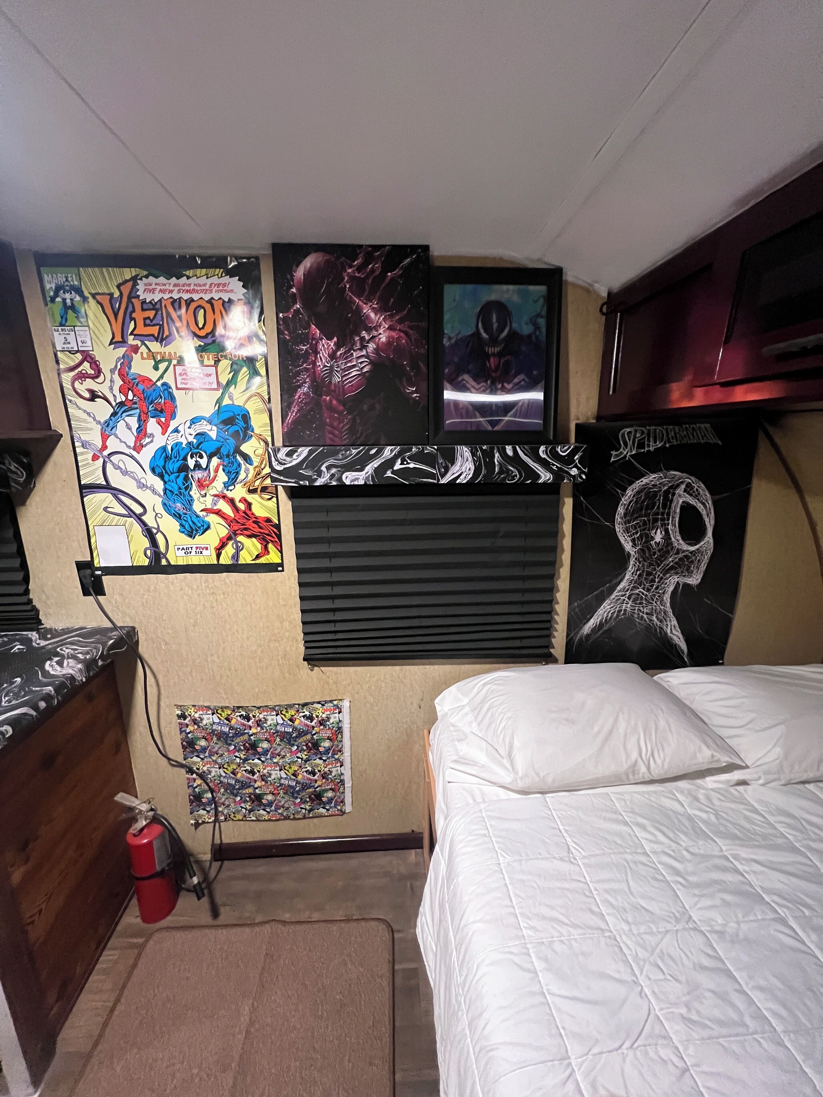 A bedroom with a bed, a wall-mounted TV, and various posters.