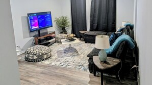 Ett vardagsrum med en platt-TV, en soffa, ett soffbord, en lampa och en krukväxt.