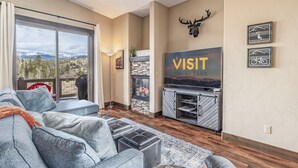 A living room with a large window, a fireplace, a mounted deer head, and a 'VISIT' sign. - Meadow View Townhome with Hot Tub (Fraser)
