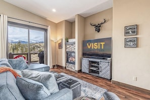 A living room with a large window, a fireplace, a mounted deer head, and a 'VISIT' sign. - Meadow View Townhome with Hot Tub (Fraser)