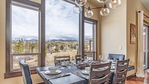 A dining area with a table set for four, large windows with a mountain view, and a chandelier. - Meadow View Townhome with Hot Tub (Fraser)