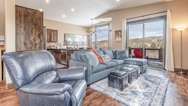 A spacious living room with a large sofa, a leather armchair, and a dining area with a kitchen in the background. - Meadow View Townhome with Hot Tub (Fraser)