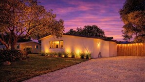Une maison de plain-pied dotée d’un éclairage extérieur soigné, d’une allée et d’une clôture en bois.