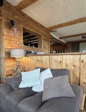 L’intérieur d’un chalet chaleureux, avec un mur en bois, un canapé confortable agrémenté de coussins et une lampe.