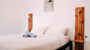 Una cama con sábanas blancas, una toalla gris y un cabecero de madera con una lámpara.