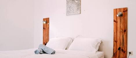 A bed with white linens, a gray towel, and a wooden headboard with a light fixture.