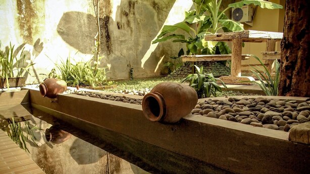 Una fuente con dos macetas de cerámica, rodeada de rocas y plantas, en un jardín.