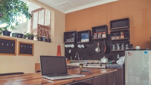 Una cocina con una computadora portátil sobre una mesa de madera, una estufa, estantes con utensilios de cocina y un refrigerador.