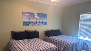 Een slaapkamer met twee bedden, een schilderij van zeilboten aan de muur en een raam met jaloezieën.