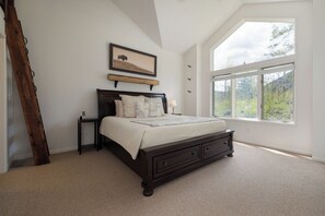 A bedroom with a large window, a wooden ladder, a bed with a quilt, and a framed picture on the wall. - Spruce Park H - Cozy East Vail Home with Private Hot Tub + Easy Village Access (Vail)