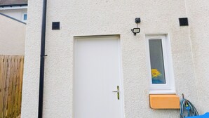 Een huis met een witte gevel, een voordeur, een klein raam en een duidelijke schoorsteen.