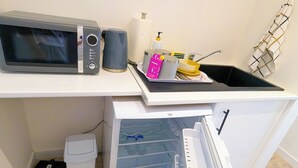 Een compacte kitchenette met een magnetron, een klein afvalbakje, een koelkast en een spoelbak.