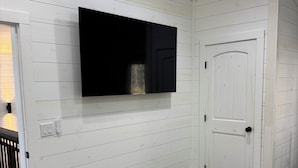 Een gang met witte houten wanden, een wandtelevisie, een deur en een kamerbreed tapijt met een patroon.