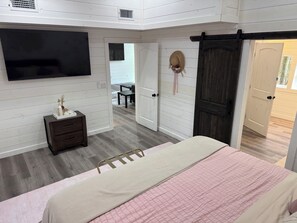 A bedroom with a bed, dresser, TV, and a door leading to another room. - Gorgeous New Skyfall Cabin in Broken Bow Sleeps 10 in Style with Huge Deck! (Broken Bow)