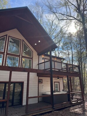 Uma cabana de dois andares com janelas amplas, varanda e um deck.