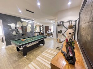 Ein modernes Wohnzimmer mit Billardtisch, einem Holztisch mit Dekoration und einem Bücherregal.