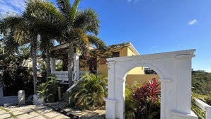 A courtyard with a white archway, palm trees, and a building with a yellow facade. - Romantic Private Pool Suite with outdoor tub Rincon, close to beaches (Rincon)