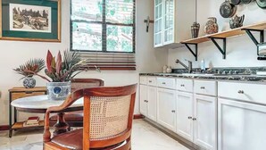A kitchen with white cabinets, a wooden chair, a round table, a potted plant, and a window with blinds. - Romantic Private Pool Suite with outdoor tub Rincon, close to beaches (Rincon)
