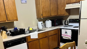 A kitchen with wooden cabinets, a dishwasher, a microwave, an oven, and a table with a chair.