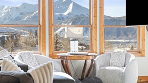 A cozy room with large windows offering a mountain view, a comfortable chair, and a table with a lamp. - Black Bear Lodge #303 | Walk to West Wall Lift, Heated Garage + Hot Tub | 2BR (Crested Butte)